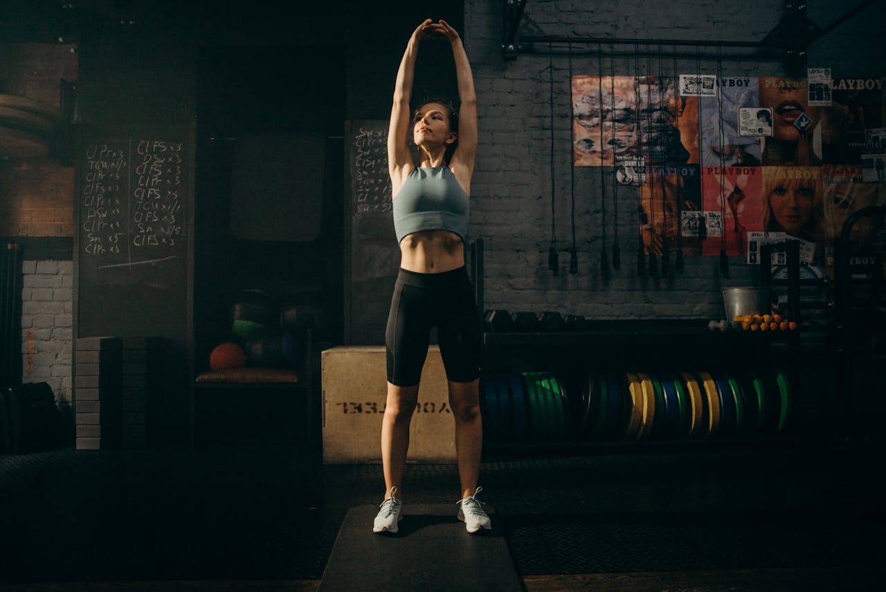 story-02 Strong woman stretching her arms in an industrial-style gym environment with motivational wall art.